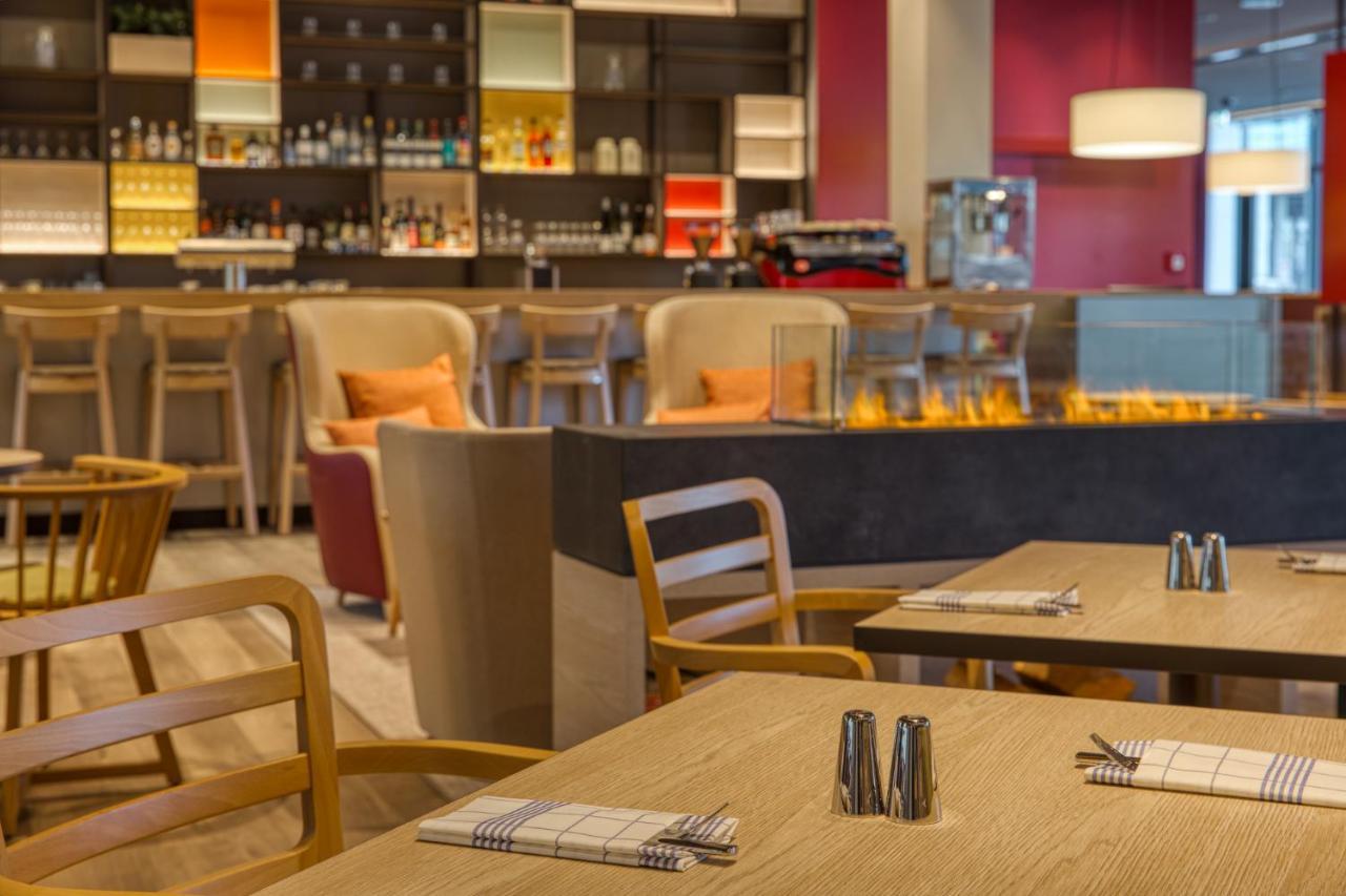 Intercityhotel Berlin Airport Ber Terminal 1 & 2 Schoenefeld Ngoại thất bức ảnh The photo shows a modern restaurant or bar interior. In the foreground, there are wooden tables set with napkins and condiments. The seating includes wooden chairs and plush seating in various colors in the background. A stylish bar area is visible w